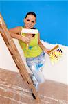 Young female worker with color guide and paint roller near the ladder