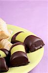 Swedish marzipan and chocolate rolls and danish macaroon fingers on a green plate over a pink background. With copy-space