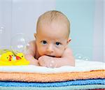 Little cute baby boy with soap bubbles lying on colorful towels