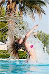 slim woman is jumping and throwing wet hair back in swimming pool