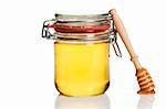honey covered honey dipper leaning at a honey jar on white background