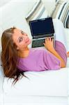 Smiling young woman sitting on sofa at home and using laptop