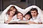 Parents with children under the blanket with a book