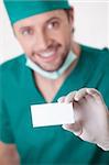A young surgeon holding a blank business card is isolated