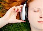 Redhead girl listening music at green grass.
