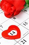 Red heart shape marker and rose on calendar page showing Febraury 14 Valentine's day