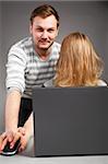 handsome man is helping weird woman with hair on face to work with laptop