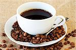 Cup of fresh brewed coffee with roasted coffee beans on straw placemat