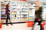 Blurred motion of people walking near refrigerator in shopping centre with baskets