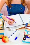 Girl sitting at table with lots of books and doing homework. Close-up