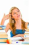 Stressful young girl sitting at table with books and holding gun shaped hand near head