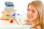 Smiling teen girl sitting at table with books