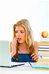 Shocked  teen girl sitting at table with books and looking on laptop