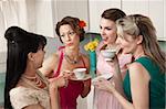 Four retro-styled women chit-chat over coffee in a kitchen