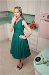 Forgetful middle-aged Caucasian woman with hand on hip in retro-styled kitchen scene