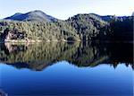 A deep blue lake reflects the gentle slopes of peaceful mountains.