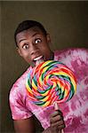 Excited African-American tastes an oversized colorful lollipop