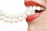 woman smiles showing white teeth, holding a pearly necklace in to the mouth, teeth care concept