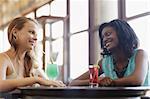 african and latin american female friends drinking cocktails and talking in a pub. Horizontal shape, side view, waist up