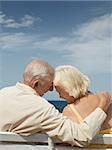 senior caucasian couple sitting on bench near the sea and hugging. Vertical shape, rear view, copy space