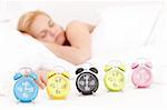 Beautiful young woman is sleeping in the bed, with many alarm clocks in the front