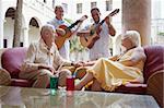 senior caucasian couple sitting in bar at hotel and listening to musicians playing guitar. Horizontal shape