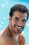 Handsome happy young hispanic man smiling and relaxing near hotel pool. Vertical shape, head and shoulders