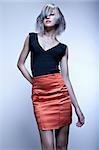 Blond fashion model with modern haircut and red skirt in studio with blue background