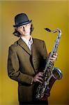 portrait of young funny man in bowler hat holding saxophone. yellow background