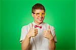 Handsome young man in a shirt and yellow glasses, bow tie on a green background smiling at the camera. Two thumbs up