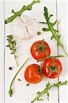 Tomatoes, arugula, garlic and thyme on a white wooden boards.