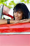 young adult brunette woman leaning on convertible red car and looking at camera. Vertical shape, front view, copy space