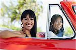 young adult brunette twin women driving convertible red car and looking at camera. Horizontal shape, side view