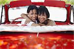 young adult brunette twin women driving convertible red car and looking over shoulders. Horizontal shape, rear view, copy space