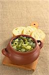 Green bean and potato hotpot in rustic bowl with baguette slices on wooden board (Selective Focus, Focus on the first half of the hotpot)