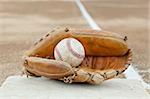 An old worn baseball in a baseball glove on a base