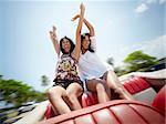 young adult brunette twin women sitting in convertible red car and laughing. Horizontal shape, front view, copy space