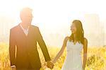 Bride and Groom holding hands, surrounding by natural morning golden sunlight.