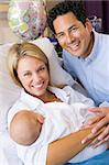 New mother with baby and husband in hospital smiling