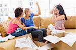 Three girl friends playfully unpacking boxes in new home smiling