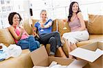 Three girl friends relaxing with champagne by boxes in new home