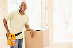 Man wearing tool belt standing by boxes in new home smiling