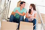 Couple sitting on staircase with boxes in new home smiling