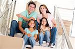 Family sitting on staircase with boxes in new home smiling