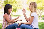 Two young girl friends sitting outdoors playing patty cake smili