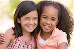 Two young girl friends sitting outdoors smiling