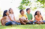 Five young friends sitting outdoors with soccer ball looking up