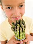 Young girl holding bunch of asparagus and smiling