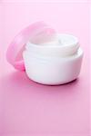 Container of cosmetic moisturizing cream on pink background.