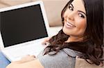 Beautiful happy young Latina Hispanic woman smiling and using a laptop computer at home on her sofa